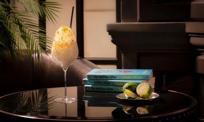 Photo of a posh cocktail beside a pile of books, and a dish of cut limes. All very tasteful and expensive looking.