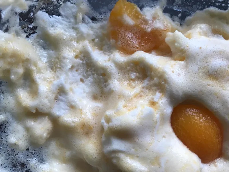 Close-up photograph of a frothy pudding, streaks of orange and white, canned apricots half-submerged.