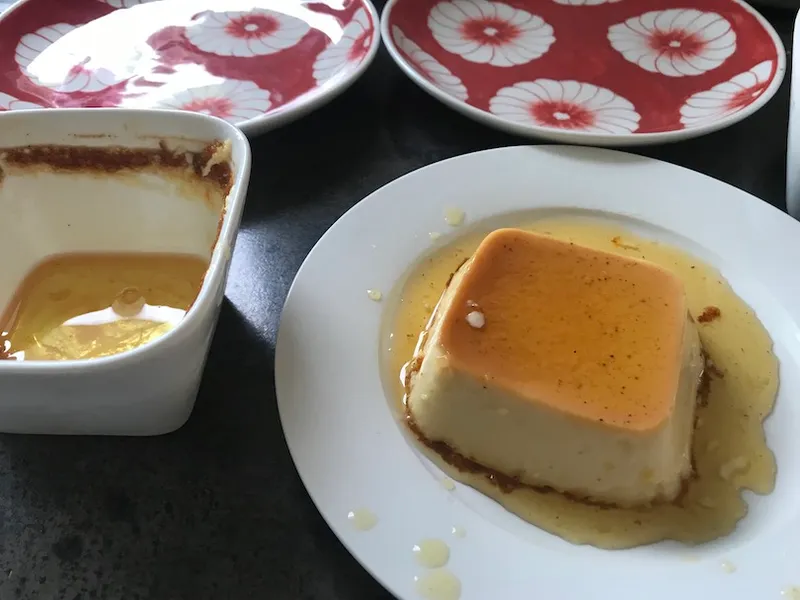 A ramekin with a layer of shiny golden stuff in the bottom, next to a plate holding a square custard swimming in golden liquid.