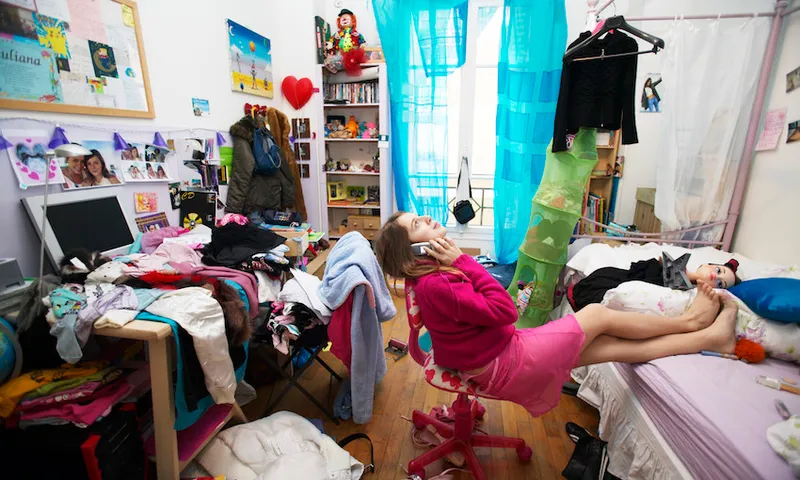 Young Woman Sits on a Chair in a Messy Bedroom Using a Mobile Phone