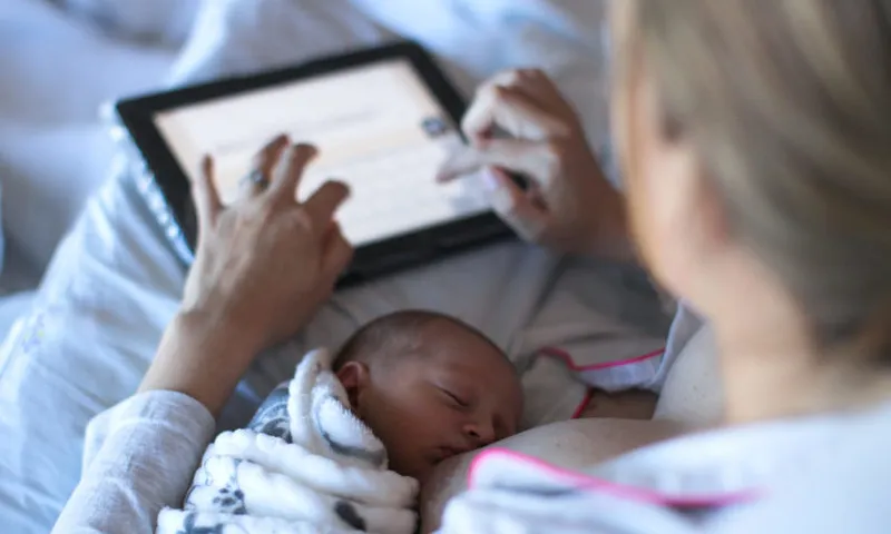 a Young woman fills in a revue of the hospital she gave birth in on a digital tablet while breastfeeding.