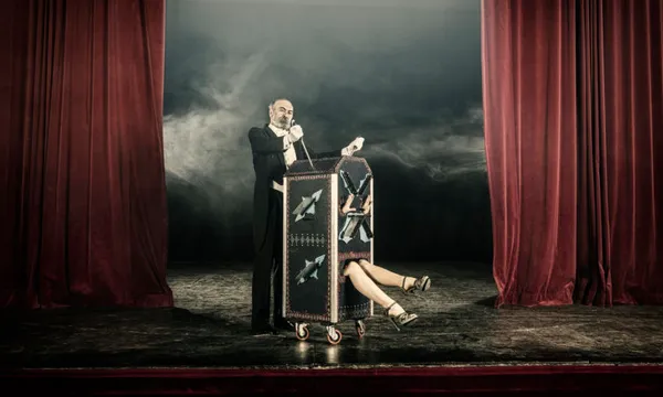 Magician inserting swords in box occupied by female assistant
