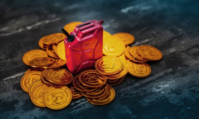 High Angle View Of Miniature Red Gasoline Gallon And Gold Coins On Table