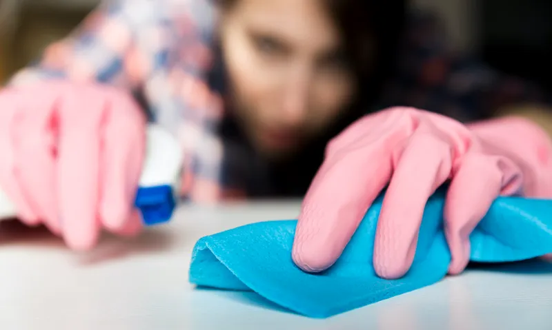 Woman in protective gloves is diligently cleaning white surface using a spray and a duster, cloth