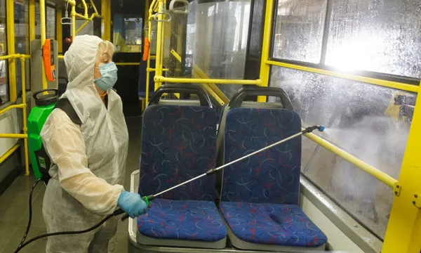 A worker wearing protective gear, sprays disinfectant to