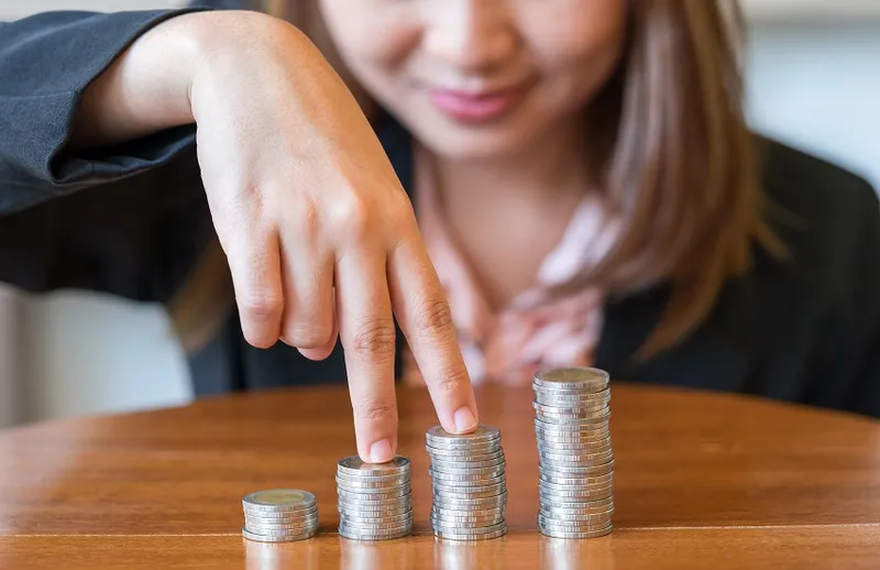Midsection Of Businesswoman Sitting By Stacked Coins At Desk