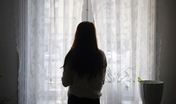 Rear View Of Woman Looking Through Window While Standing At Home