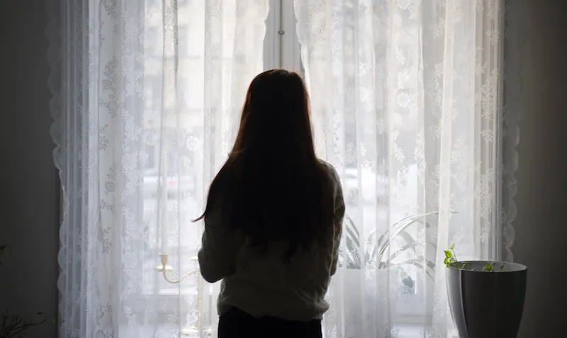 Rear View Of Woman Looking Through Window While Standing At Home