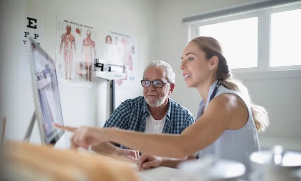 Female doctor showing computer to senior male patient in examination room