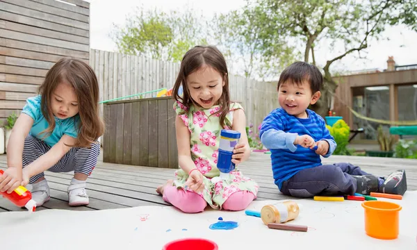 Three young children painting and drawing in garden