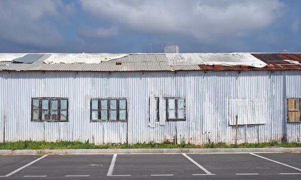 an old abandoned white industrial building with rusting patched repaired corrugated roof and boarded up windows
