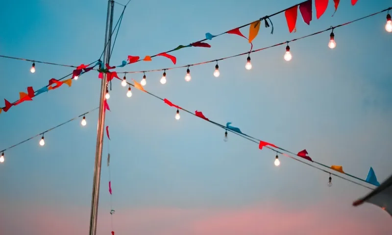 Low Angle View Of Bunting Flags And Light Bulbs Hanging Against Sky During Sunset