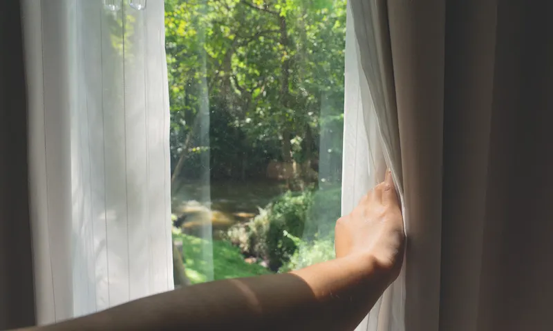 Asian female hand opening curtains with green forest view