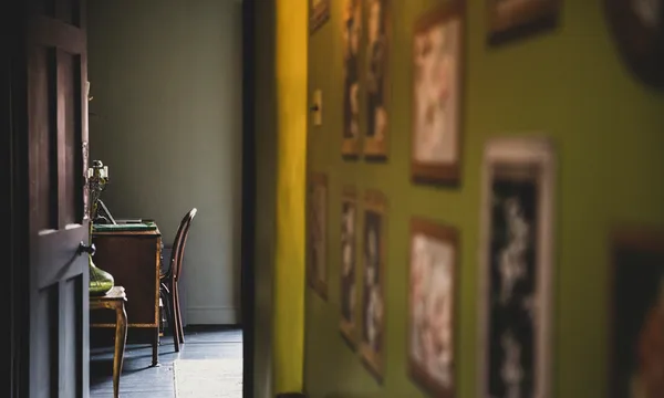 View along corridor with vintage pictures on green wall, open brown wooden door to study with antique desk and chair.