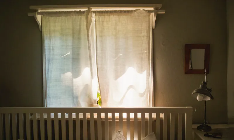 Woman asleep in bed in front of window with curtain and geranium