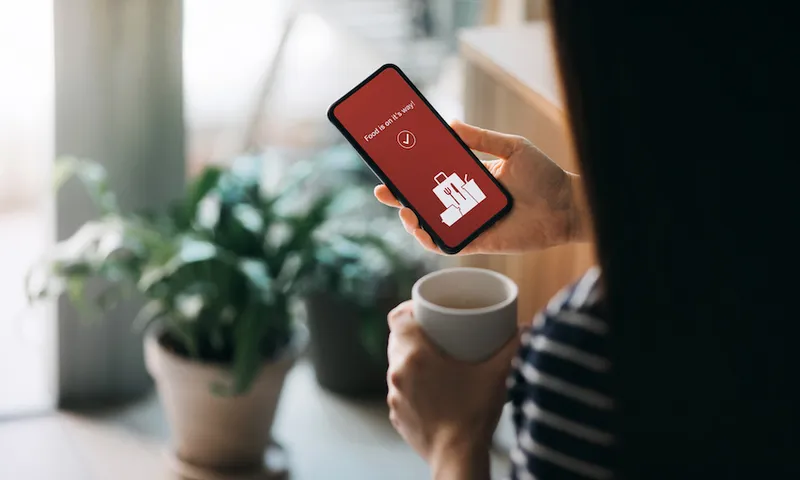 Young Asian woman using mobile app on smartphone to order food delivery online at home in self isolation during the Covid-19 health crisis