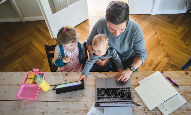 High angle view of man using laptop while sitting with cute son by daughter looking at digital tablet
