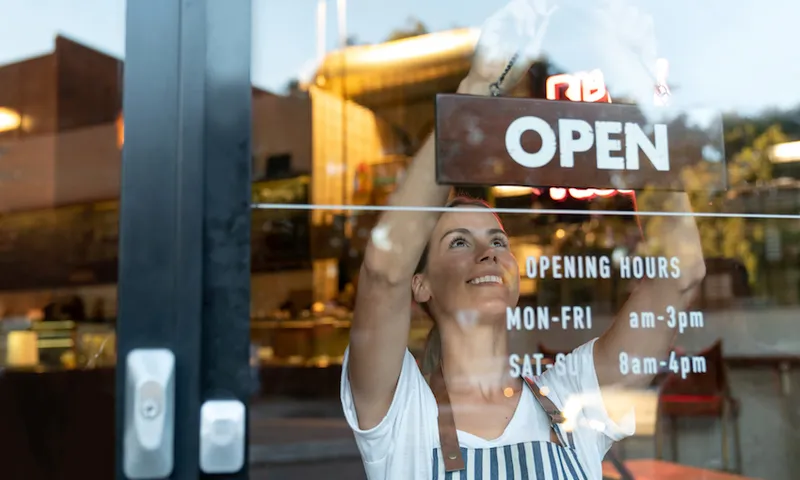 Happy business owner hanging an open sign at a cafe