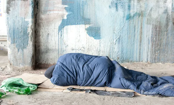 Homeless man sleeping in sleeping bag on cardboard