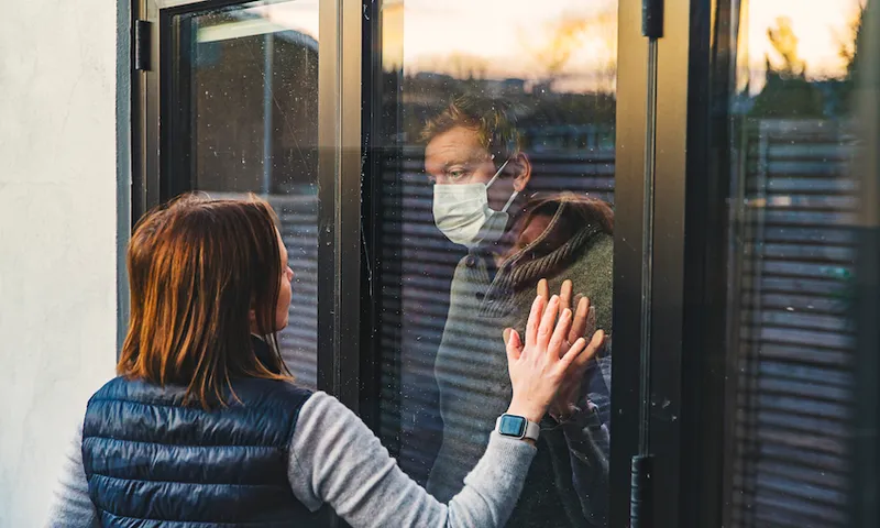 Woman looking at masked husband quarantined behind window