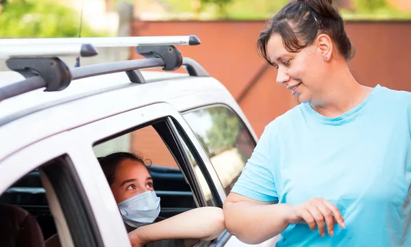 Female family members wearing masks performing Covid-19 elbow bump greeting through car window