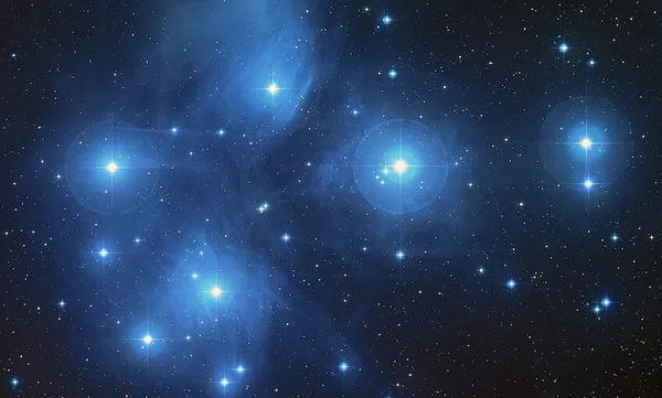 A starry night sky featuring the Pleiades star cluster, with several bright blue stars surrounded by faint clouds of gas and dust, set against a backdrop of smaller twinkling stars.