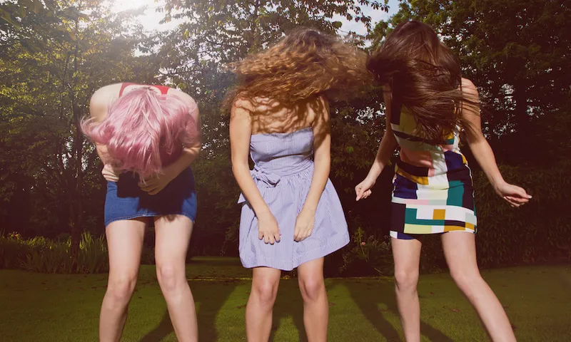 Excited female friends tossing hair at yard during sunny day