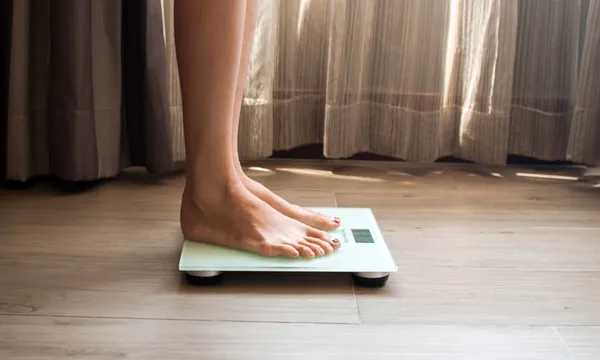 A young woman is weighing herself in a weighing scale