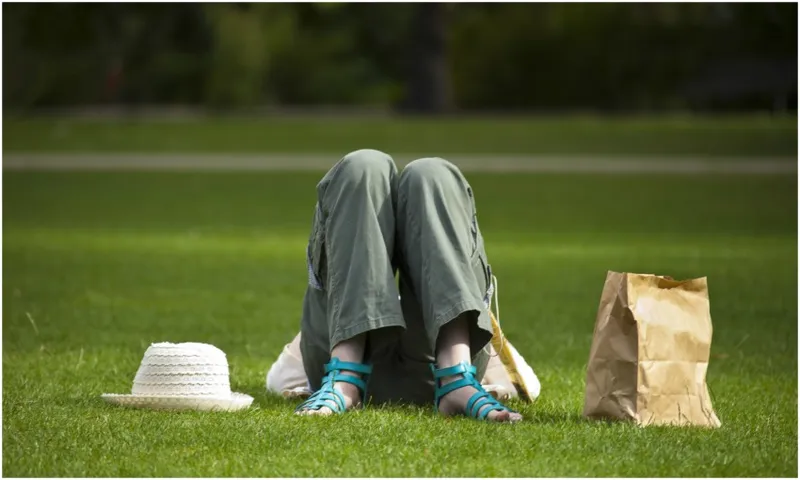 Person lying on their back on grass, we see their bent knees, a hat and paper bag beside them.