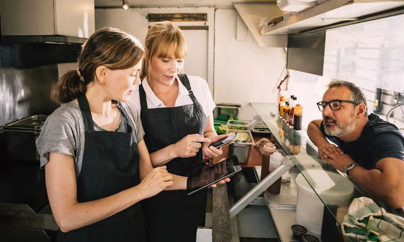 Female chefs with technologies while receiving order from man in food truck