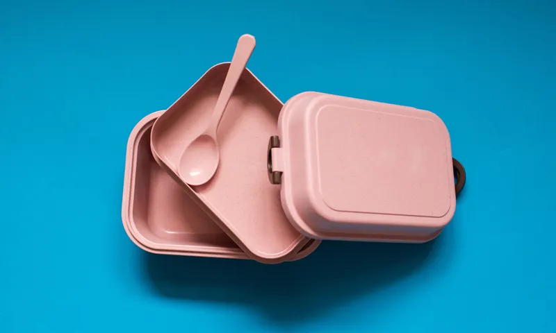 Empty pink bento lunch box with spoon on blue background