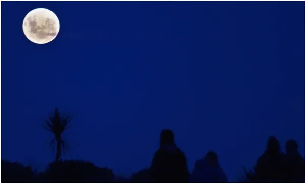 a few buildings and rocks outlined against deep blue twilight with a normal moon in the corner