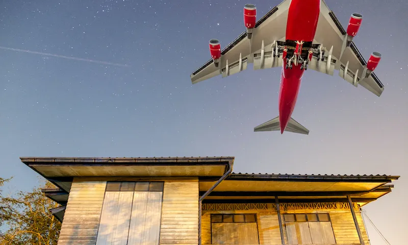 Big passenger plane over wooden house in countryside