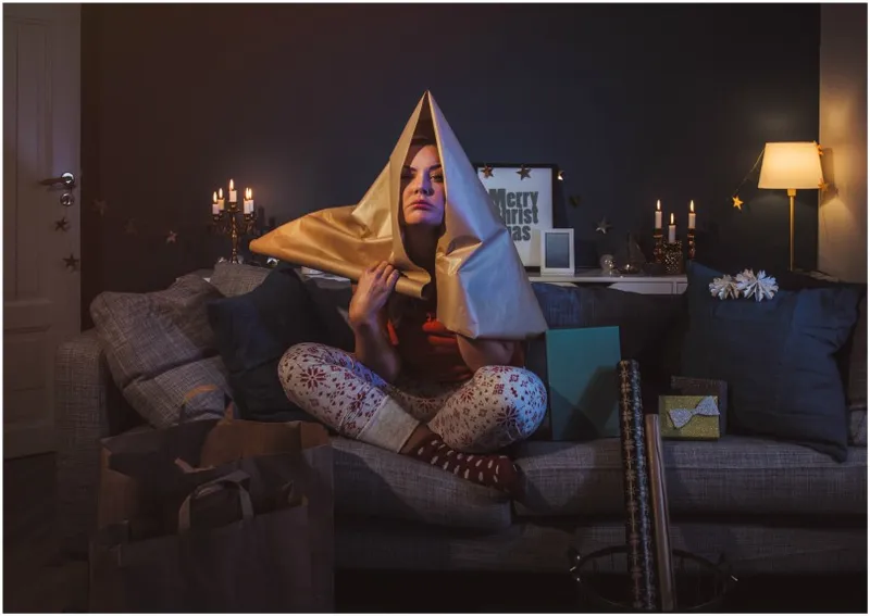 Woman on couch with wrapping paper over head, looking stressed