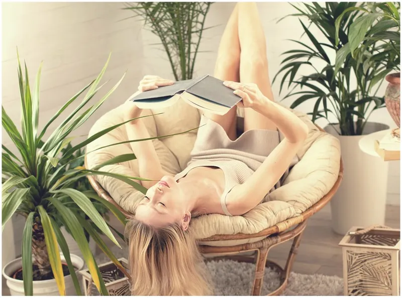 woman lying head-down on chair, holding book above her head to read