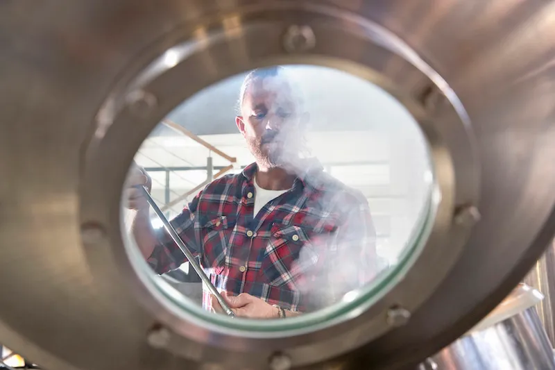 Male Brewery Worker Checking Fermentation Process In Steel Vat