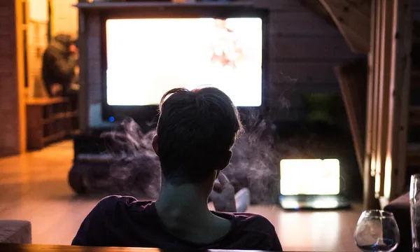 Rear View Of Man Smoking While Watching Television At Home