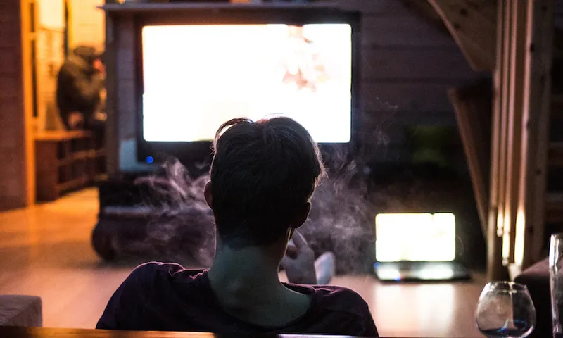 Rear View Of Man Smoking While Watching Television At Home