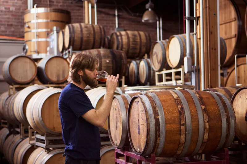 Side view of brewer tasting beer while standing in warehouse