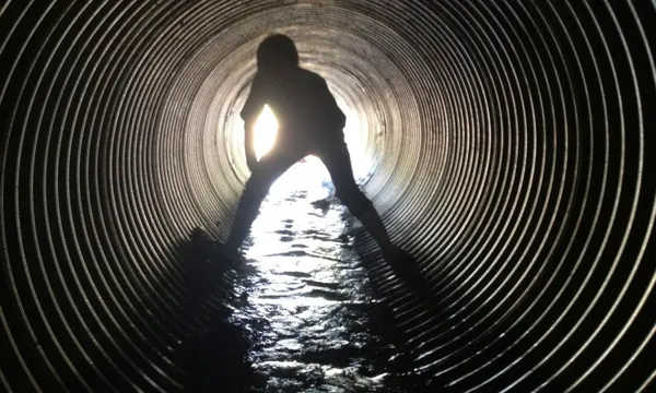 Rear view of silhouette boy standing in sewage tunnel