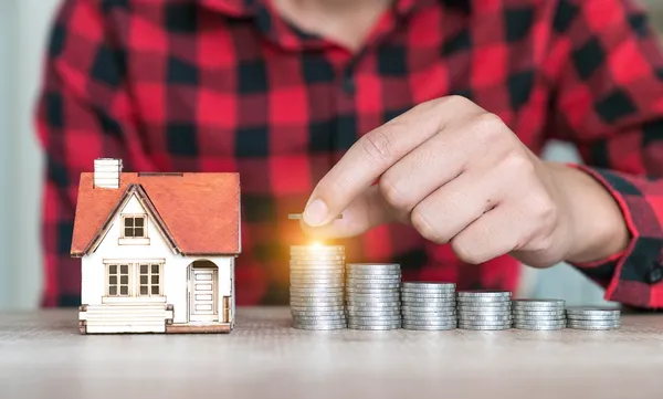 hand putting coin with house model background, gold coins stack on wooden table in the morning sunlight. business, investment, retirement, finance and Money Saving for the future concepts