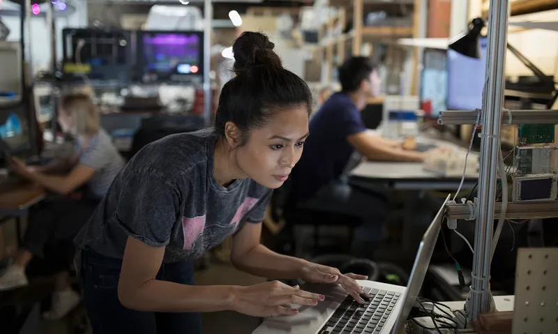 Focused female engineer working at laptop in workshop