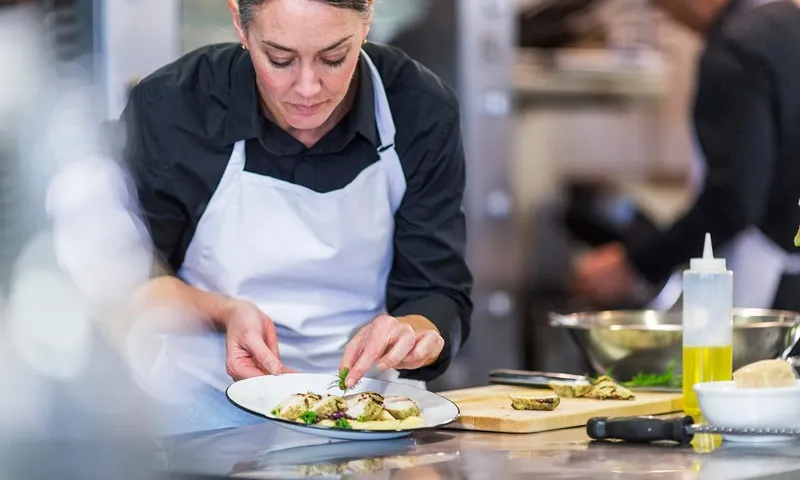 Female chef garnishing food while coworker working in background at restaurant