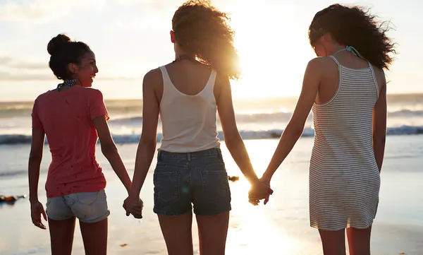 Three young women standing by the sea, hand in hand
