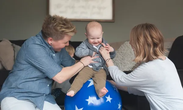 Lesbian Mothers Play with Baby on a Ball with Stars in Their Home