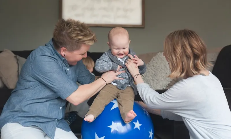 Lesbian Mothers Play with Baby on a Ball with Stars in Their Home