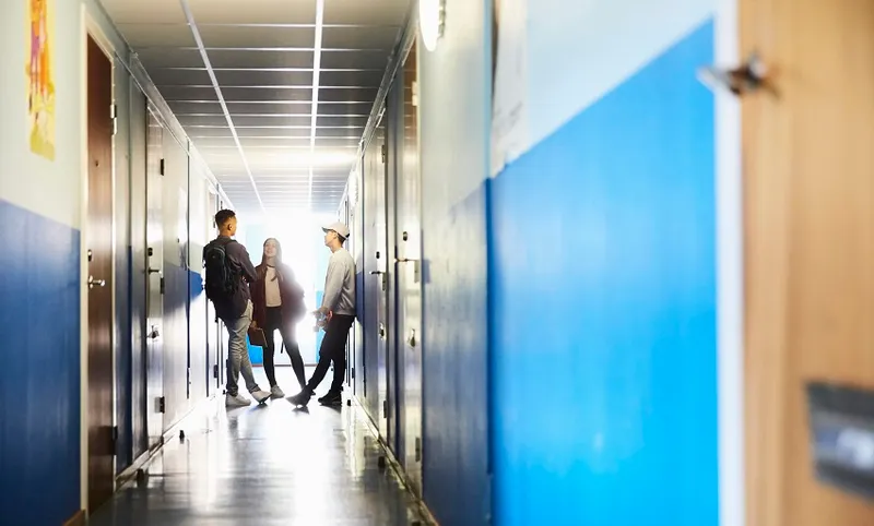 Full length of students talking while standing in corridor at university