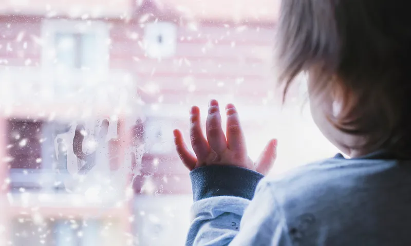Little boy looking out of the window on a snowy day