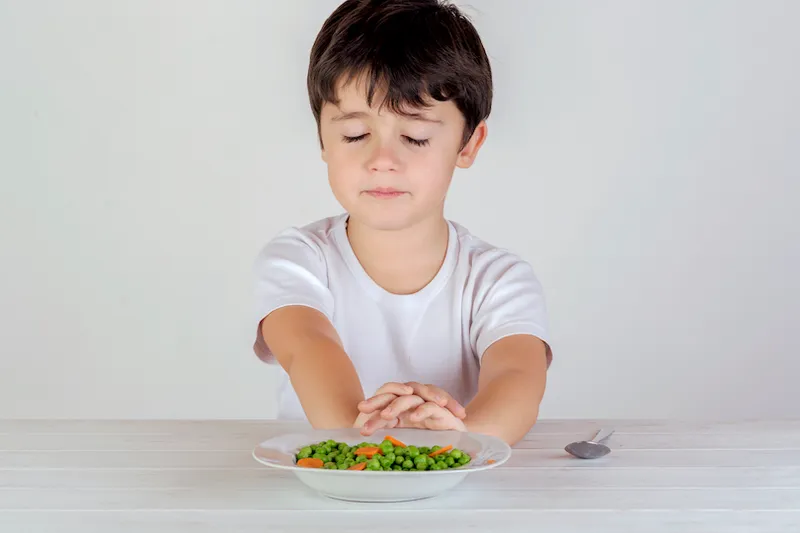 Unhappy Caucasian boy eating vegetables