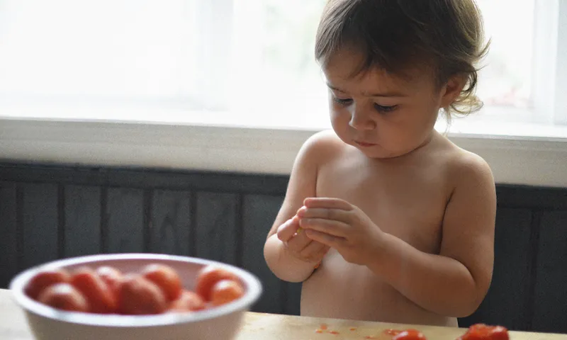 Toddler girl in the kitchen with tomatoes.